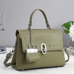 Olive green leather handbag detail, metal clasp and mini bag charm, textured surface.