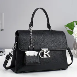 Detailed view of black litchi leather handbag with metal clasp and miniature bag charm.