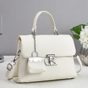 Close-up detail of white leather handbag with metal lock and mini charm pendant.