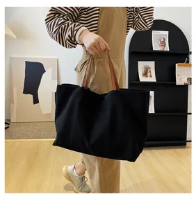 Large canvas tote bag detail view, casual black shoulder bag with brown leather handles.