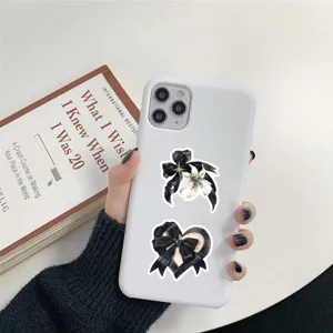 White phone case with gothic black ribbon and flower stickers, aesthetic daily phone accessory.