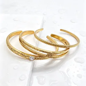 Detail shot of gold plated open cuff bracelets with delicate leaf engraving and sparkling gemstone.