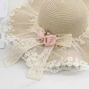 Beiger geflochtener Strohhut mit weißer Spitzenborte und rosa Rosen für den Sommer am Strand.
