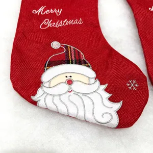Close-up detail of embroidered red Christmas stocking with Santa Claus face and festive text.