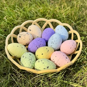 Close-up detail of colorful speckled Easter eggs in a yellow basket on green grass decor.