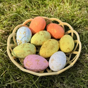 Close-up of colorful Easter eggs with gold foil speckles in a yellow basket on green grass.
