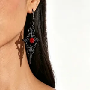 Boucle d'oreille poignard métal noir gothique avec pierre rouge, détail bijou gros plan.