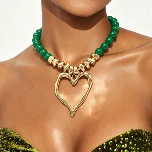 Gros plan détaillé des perles en acrylique vert et du pendentif cœur doré irrégulier.