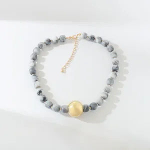 Stilvolle Resin Perlenkette in Schwarz-Weiß-Marmoroptik mit auffälligen goldenen Akzentkugeln.