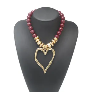 Collier statement chic en perles acryliques bordeaux avec grand pendentif cœur doré asymétrique.
