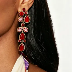 Close-up detail shot of exaggerated long red crystal rhinestone drop earrings in gold setting.