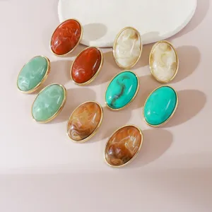 Detailed close-up of oval resin inlay earrings with multicolor marbled patterns and gold metal rims.