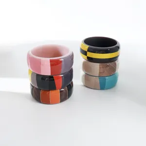 Vista dettagliata di bracciali rigidi in acrilico color block con motivi a righe e a quadri.