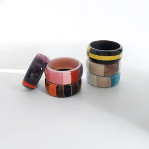 Vista dettagliata di ampi bracciali in resina acrilica color-block con motivi a righe e geometrici.