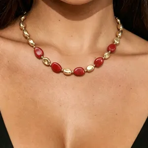 Dettaglio di una collana statement dorata e rossa con perle organiche dal design unico.