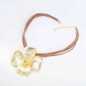 Detailopname van een grote gouden bloemhanger aan een stijlvolle bruine snoer ketting.