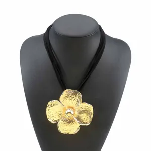 Gedetailleerde opname van de oversized gestructureerde gouden bloemhanger ketting met fluwelen koord.