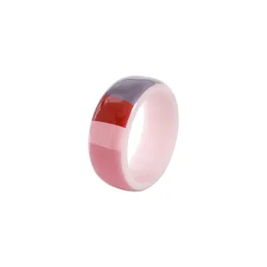 Primo piano di un anello in acrilico colorato con motivo a blocchi rosa, rosso e viola.