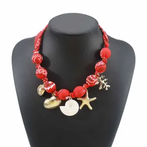 Detailaufnahme der roten Stoffperlen Halskette mit goldenen Meeresanhängern und Muscheln.