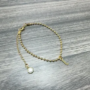 Elegante goudkleurige kralenketting armband met letterhanger en sprankelende strass steen.