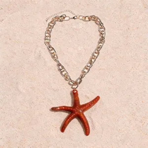 Close-up detail shot of the resin starfish pendant and chunky metal chain on sandy background.