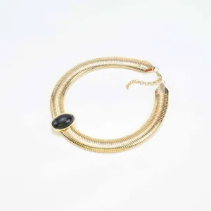 Closeup of wide gold snake bone chain choker with black oval stone and metallic finish.