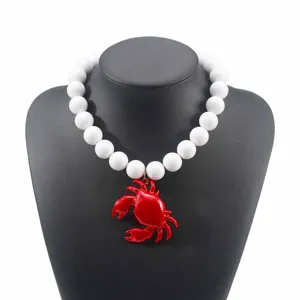 Collana di perle bianche spesse con ciondolo granchio rosso, dettaglio di gioielli costieri.
