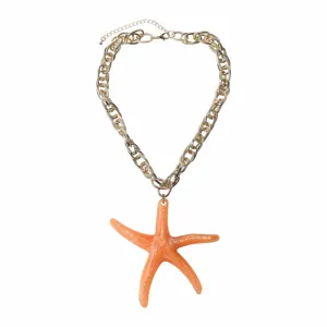 Close-up detail of the chunky gold chain necklace featuring a large vibrant orange resin starfish.