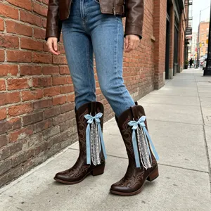 Detailed view of brown western cowboy boots featuring blue bow and pearl chain accessories.