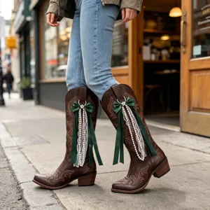 Brown western cowboy boots decorated with green bow ribbons, lace, and pearl strands for stylish outfits.