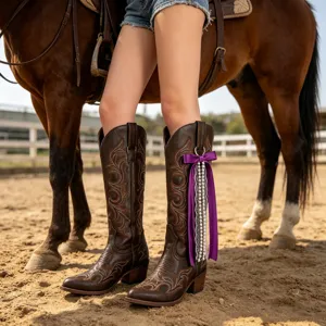 Gros plan de bottes de cowboy marron foncé avec ruban violet et pendentif perlé en ranch.