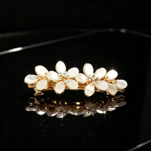 Detail of gold metal hair clip with white cat-eye stone flowers and sparkling rhinestones.