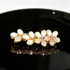 Elegant gold-tone rhinestone floral hair clip with white cat-eye stone petals, detail view.