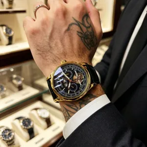Luxury men's automatic mechanical watch with gold case, black dial and leather strap.