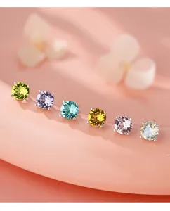 Gros plan de boucles d'oreilles clous en zircone ronde coloree sur fond rose doux.