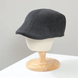Detailed closeup of dark grey herringbone wool ivy flat cap displayed on wooden stand.
