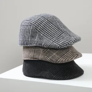 Vue rapprochée détaillée de trois casquettes plates à carreaux empilées gris marron noir.