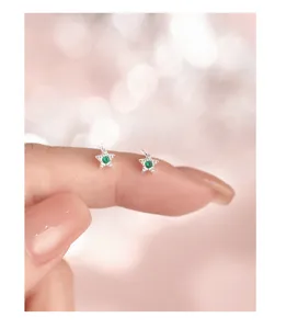 Nahaufnahme zarter Stern-Ohrstecker mit leuchtend grünen Zirkoniasteinen am Finger.