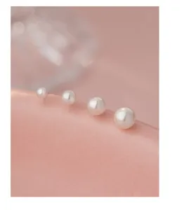 Detailaufnahme weißer Perlen-Ohrstecker in verschiedenen Größen, minimalistisch elegant.