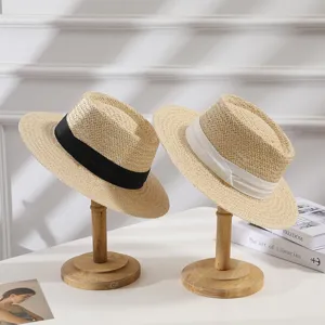 Detail view of stylish flat top straw hats with ribbons displayed on wooden stands for summer.