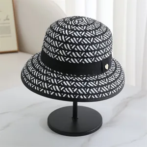 Vue détaillée d'un élégant chapeau de pêcheur tissé noir et blanc avec ruban et bijou.