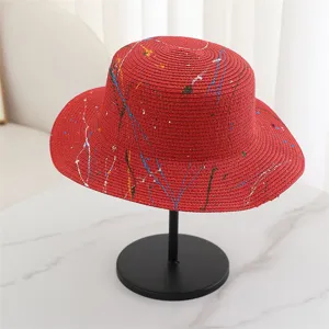 Detailed view of red flat-top straw sun hat with colorful graffiti splash paint design.