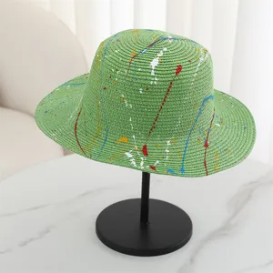 Close-up detail of green straw hat with colorful paint splatter design for summer outdoor wear.