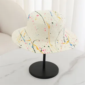 Close-up of flat top straw hat with colorful paint splatter design for summer beach wear.