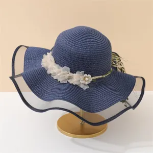 Dunkelblauer, breiter Strohhut Detail, mit weißen Stoffblumen und schwarzem Netzkantendetail.