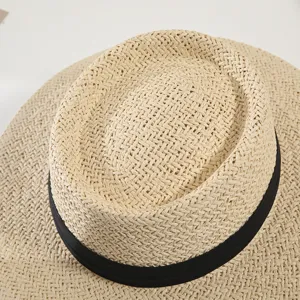 Close-up detail of beige flat-top straw hat with chic black ribbon for summer sun protection.