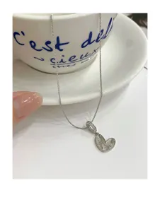 Detailansicht der silbernen Herzanhänger Halskette auf weißem Hintergrund mit Dekotasse.