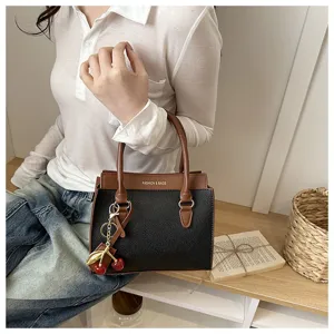 Detail view of a stylish color block handbag with a cute cherry charm held by a model.