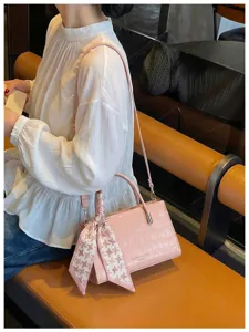 Chic pink embossed leather shoulder crossbody bag featuring a stylish ribbon accessory detail.