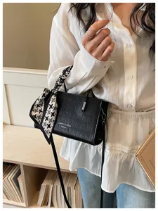 Black crocodile pattern shoulder bag detail, elegant square handbag with scarf accessory.